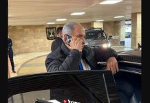 φωτογραφία δείχνει τον Benjamin Netanyahu να μιλά σε κινητό με κόκκινη ταινία στις κάμερες.