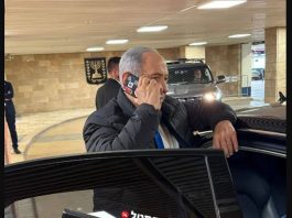 φωτογραφία δείχνει τον Benjamin Netanyahu να μιλά σε κινητό με κόκκινη ταινία στις κάμερες.