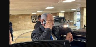φωτογραφία δείχνει τον Benjamin Netanyahu να μιλά σε κινητό με κόκκινη ταινία στις κάμερες.