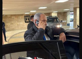 φωτογραφία δείχνει τον Benjamin Netanyahu να μιλά σε κινητό με κόκκινη ταινία στις κάμερες.