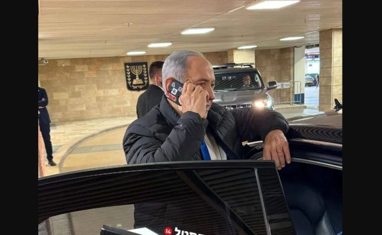 φωτογραφία δείχνει τον Benjamin Netanyahu να μιλά σε κινητό με κόκκινη ταινία στις κάμερες.